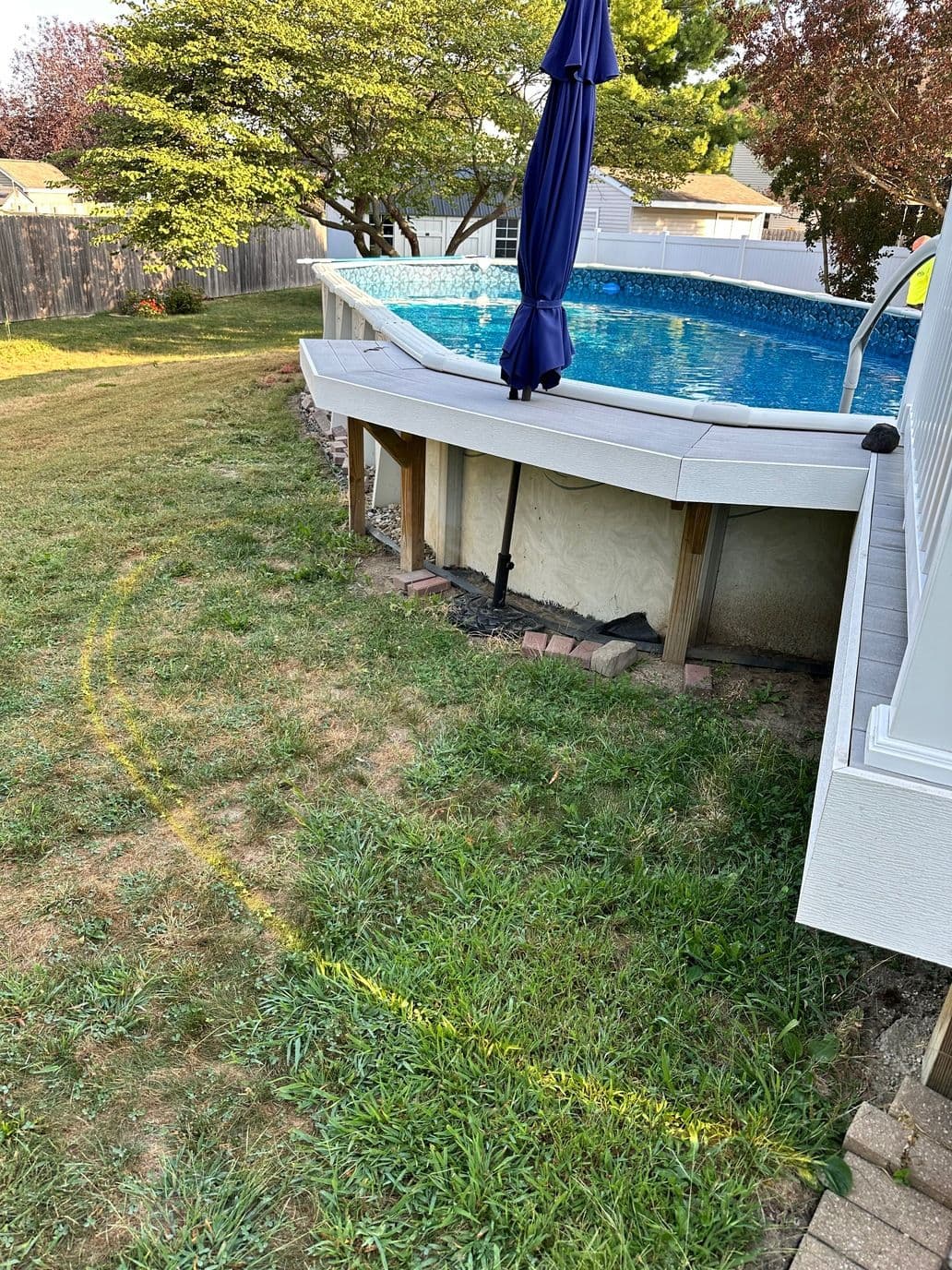 Inground pool with blue water surrounded by grass and landscaping in a backyard setting.